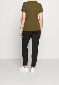 T-shirt verde oliva a maniche corte con vestibilità rilassata, abbinato a pantaloni jogger neri. Sneakers bianche completano l'outfit. Tessuto morbido, design casual.