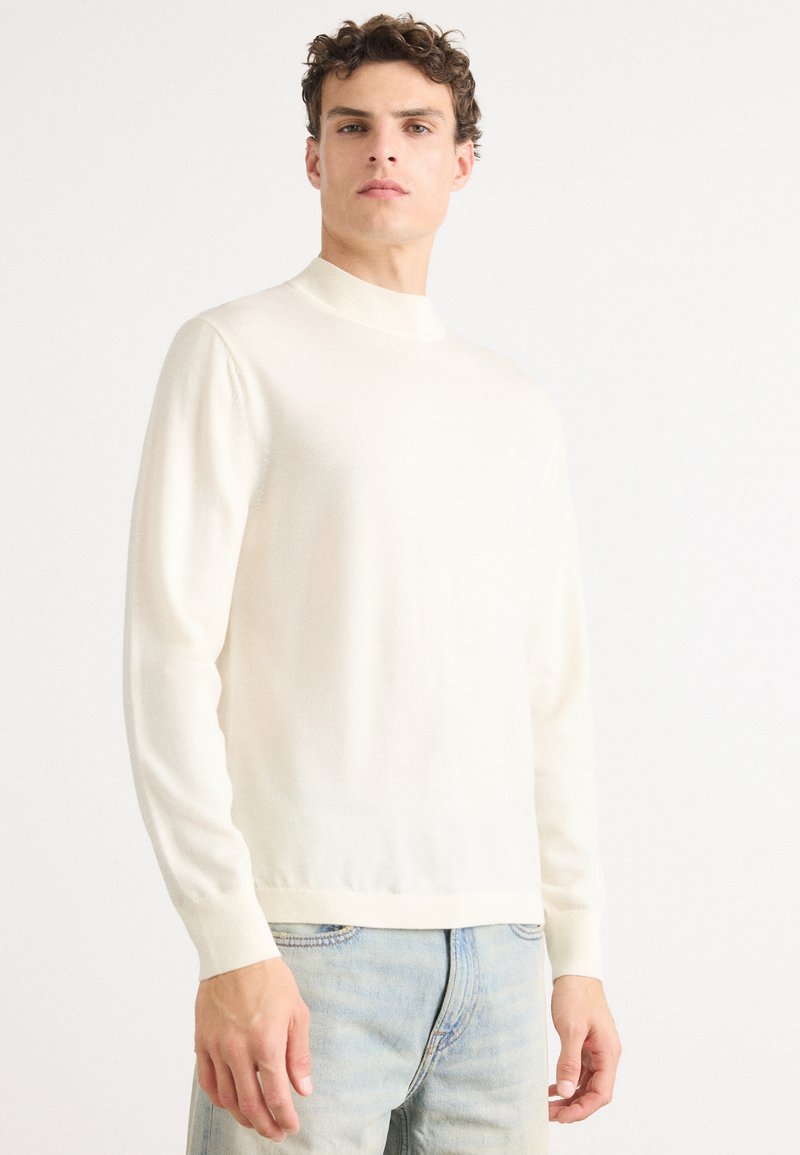 Maglione chiaro con collo alto, maniche lunghe e una texture morbida e liscia. Abbinate a jeans azzurri per un contrasto.