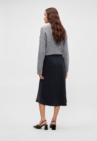 Grå strikketrøje, marineblå satin midi nederdel og sorte hælede sandaler med blokhæl. Outfittet har et strømlinet, enkelt design.