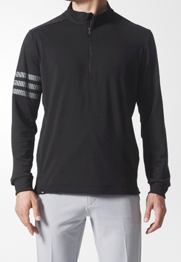 Pullover negro de mangas largas y cremallera de un cuarto con tres franjas reflectantes en el brazo derecho, llevado con pantalones gris claro.