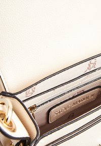 Krémová faux kůže kabelka s černými detaily, s texturovaným povrchem, zlatým kováním a vzorovaným interiérem s několika přihrádkami.