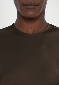 Tricou maro cu guler rotund, confecționat dintr-un material neted și elastic. Prezintă un design simplu cu mâneci scurte și detalii minime de cusătură.