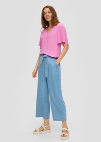 Roze V-hals top met vlindermouwen, gecombineerd met lichtblauwe wijde denim broek met een gestrikt tailleband en beige sandalen.
