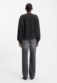 Tamsiai pilkas perdidintas džemperis su nusmukusiais pečiais, ribinėmis rankogaliais, derinamas su šviesiai pilkomis tiesiomis džinsinėmis kelnėmis su galinėmis kišenėmis.