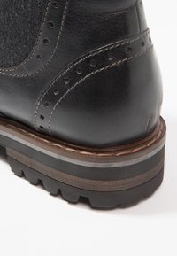 Botte en cuir noir avec une tige texturée, des perforations décoratives, et une semelle épaisse et robuste avec des accents de couleur en couches.