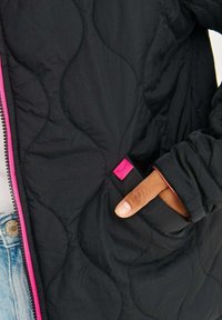 Černá prošívaná bunda s vlnkovým vzorem, růžovým zipem a malou růžovou nášivkou na kapse. Měkká, lehká tkanina.