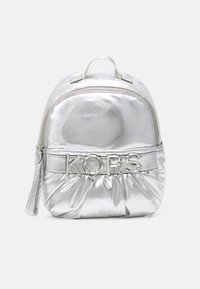 Mochila metálica plateada con textura acolchada, que cuenta con un asa superior y un zipper frontal. El nombre de la marca "KORS" se muestra de manera prominente en hardware plateado.