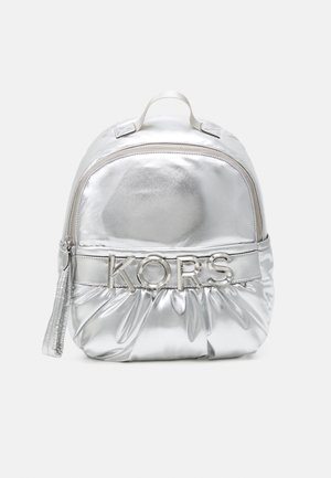 Zaino metallico argento con texture trapuntata, dotato di manico superiore e zip frontale. Il nome del marchio "KORS" è visibile in modo prominente in hardware argentato.