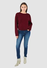 Maglione bordeaux in maglia con scollo rotondo, abbinato a jeans skinny blu e stivaletti grigio chiaro con risvolti.