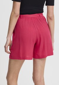 Shorts roses texturés avec une coupe décontractée, présentant une taille élastique et un tissu légèrement drapé. L'ourlet se termine juste au-dessus du genou.