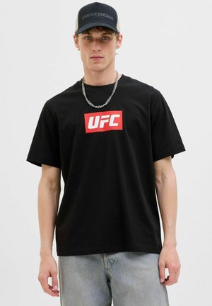 Sort bomuld t-shirt med et fremtrædende rødt UFC-logo på forsiden. Kombineret med lyseblå jeans og en sort/grå kasket. Sølv kædehalskæde.