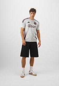 Herre grå fodboldtrøje har maroon accenter og en tekstureret design, parret med sorte shorts og hvide sneakers med røde striber.
