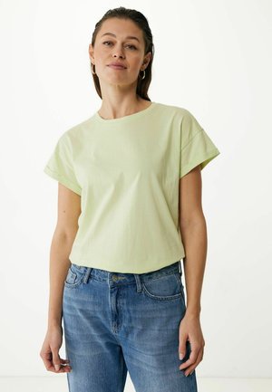 T-shirt verde chiaro a maniche corte con collo a giro, realizzata in tessuto morbido, abbinata a jeans in denim blu. Nessun motivo o dettaglio visibile.