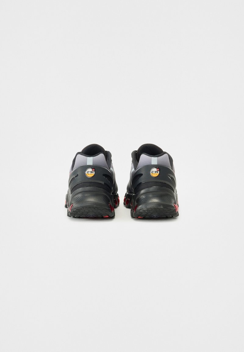 Schwarze und graue Sportschuhe mit strukturierten Gummisohlen, verstärkter Fersenstütze und roten Akzenten. Mit einem Logo an der Ferse.