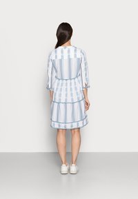 Niebieska i biała sukienka z bawełny w wzory, z rękawami 3/4, z warstwowym krojem i ozdobnym wykończeniem u dołu. Noszone są sneakersy.
