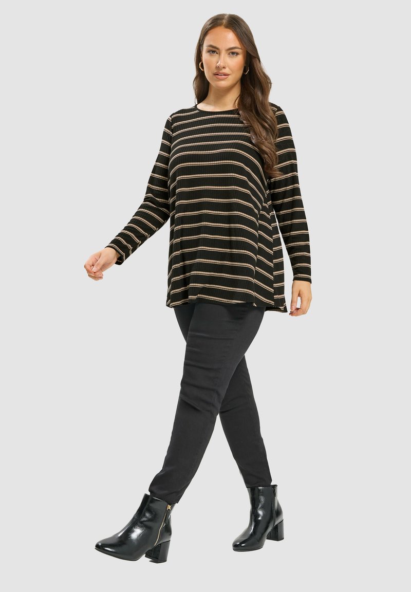 Top de manga larga a rayas negro y beige con un ajuste holgado, combinado con pantalones ajustados negros y botas de tobillo negras brillantes.