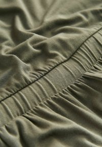 Olivgrüner Stoff mit glatter Textur, der geraffte elastische Abschnitte aufweist, die weiche Falten und Fältchen für zusätzliche Dimension zeigen.