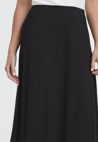 Črna maxi krila, izdelana iz mehkega, tekočega materiala. Ima gladek pas in nežen padec, brez vidnih vzorcev ali kovinskih delov.