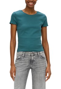 Teal-farbenes, figurbetontes T-Shirt mit kurzen, rüschengeschnittenen Ärmeln, aus weichem Baumwollmaterial, kombiniert mit hellgrauen Denim-Jeans mit distressed Details.