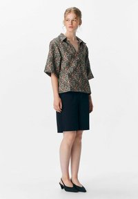 Blouse à motifs floraux avec des manches courtes et un col, associée à un short noir cintré et des chaussures à talons ouverts noires.