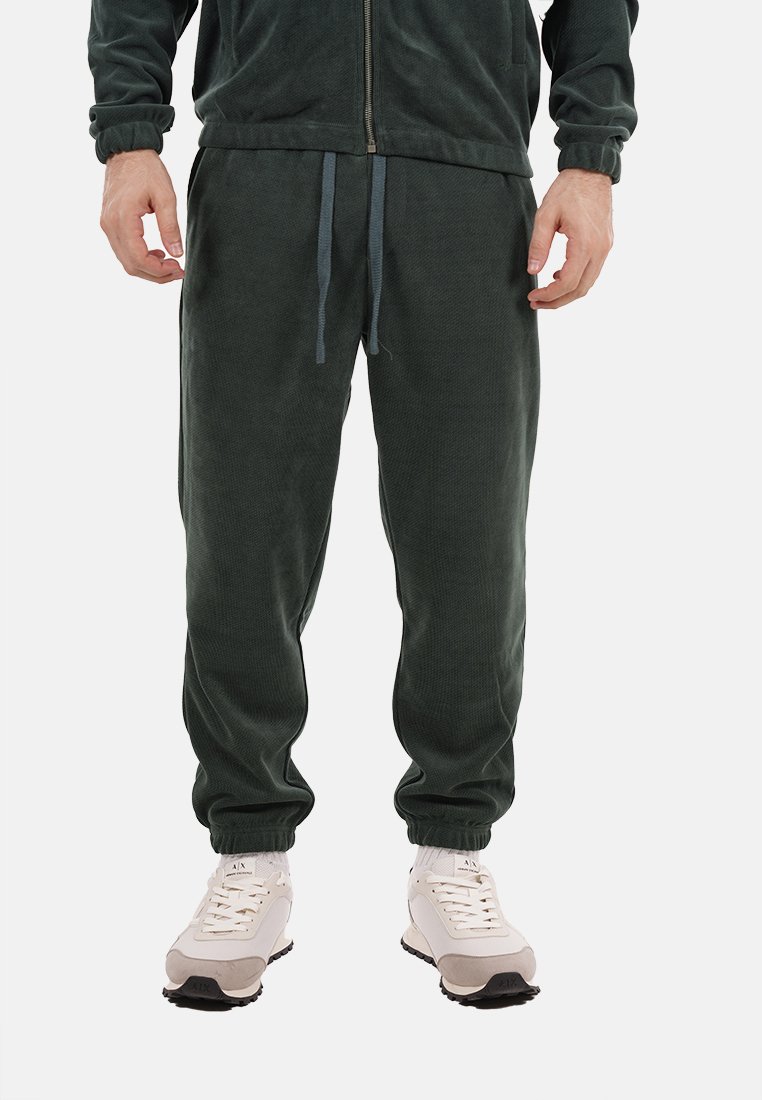 Pantaloni jogger in corduroy verde scuro con vita elasticizzata, cordoncino e gambe affusolate, abbinati a scarpe da ginnastica di colore chiaro.