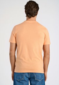 T-shirt a maniche corte arancione chiaro in morbido tessuto, con scollo rotondo e orlo dritto, indossata con jeans di denim blu.