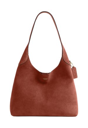 Sac d'épaule Coach en daim marron avec une poignée supérieure incurvée et une petite étiquette en cuir accrochée par une chaîne en or.