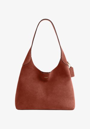 Pruun seemisnahast Coach õlakott kõverdunud ülaosaga sangaga ja väike nahast silt, mis ripub kuldse keti otsas.