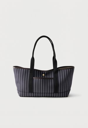 Μαύρη τσάντα tote με λευκές κάθετες ρίγες, δύο μακριές μαύρες λαβές και μια μικρή μπροστινή τσέπη με κλείσιμο κουμπιού σε χρυσό χρώμα.