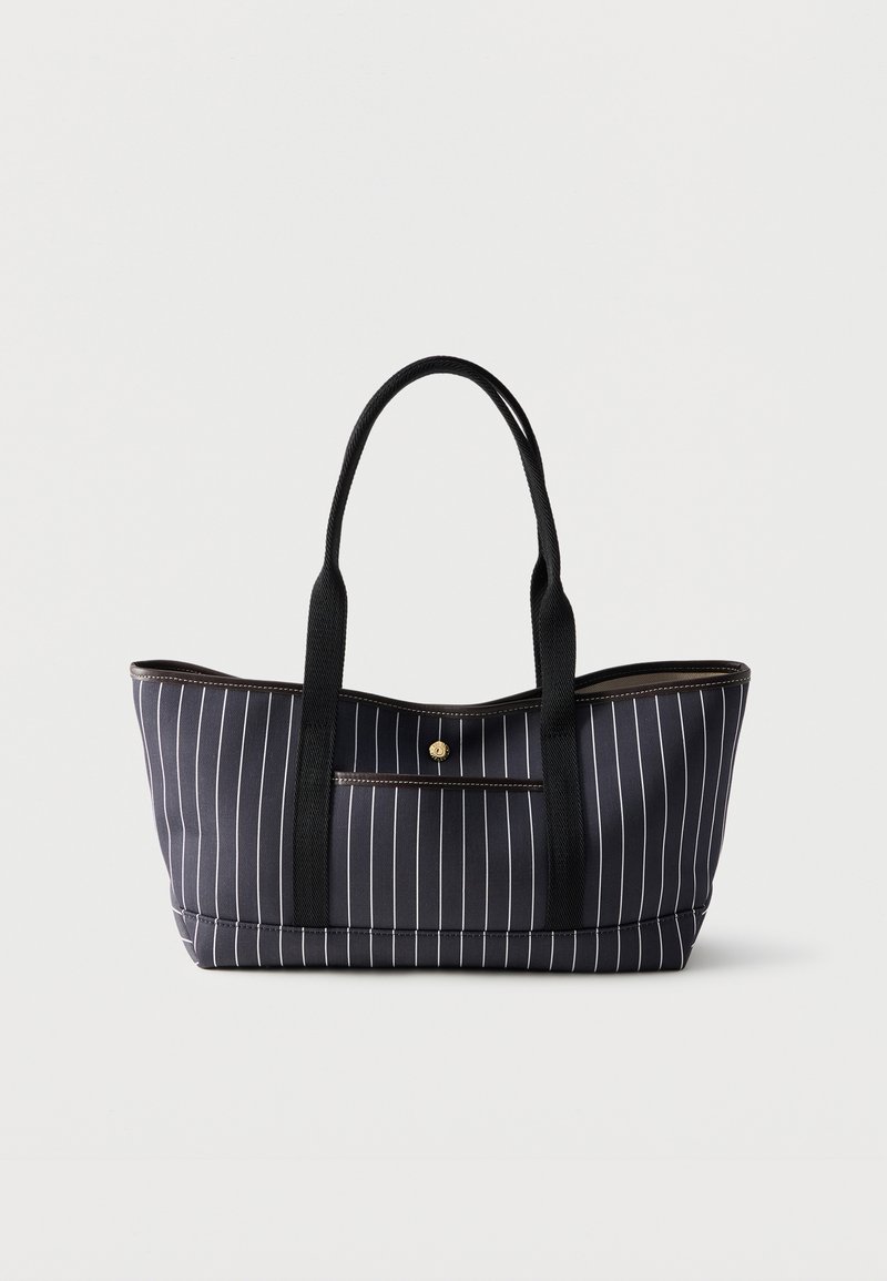 Μαύρη τσάντα tote με λευκές κάθετες ρίγες, δύο μακριές μαύρες λαβές και μια μικρή μπροστινή τσέπη με κλείσιμο κουμπιού σε χρυσό χρώμα.