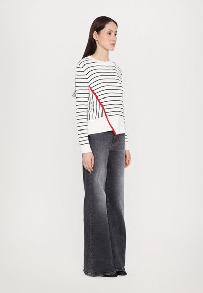Pulover dungat în alb, negru și roșu, cu mâneci lungi; asortat cu blugi gri largi; textură netedă; design minimalist.