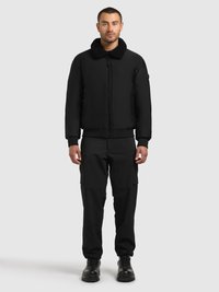 Jachetă bomber neagră cu guler plușat, fermoar frontal și manșete tricotate, asortată cu pantaloni cargo negri și cizme negre robuste.