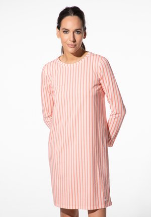 Woman with dark hair wearing a long-sleeve, knee-length dress with vertical pink and white stripes on a white background.