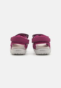 Sandalias moradas con correas ajustables de Velcro, detalles de malla y laterales perforados para transpirabilidad. Suelas sólidas blancas y texturizadas.
