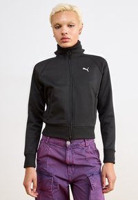 Black zip-up jacket with a high collar, features white shoulder stripes and a small white logo on the chest, made from a smooth fabric.