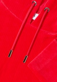 Haut à capuche en tissu rouge à côtes avec cordons assortis dotés de embouts et œillets en métal argenté, et une étiquette de taille visible "L."