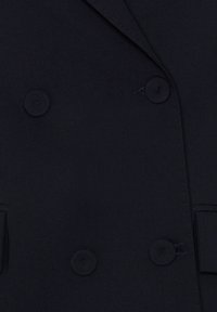 Gros plan d'un blazer noir croisé avec des boutons recouverts de tissu et des bords de revers visibles.