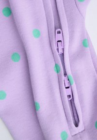 Gros plan sur un tissu lavande à pois verts avec une fermeture éclair lavande partiellement ouverte.