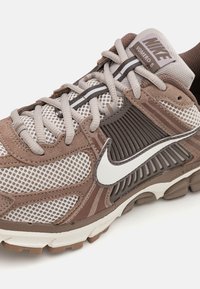Nike Vomero 5 αθλητικά παπούτσια τρεξίματος με καφέ και μπεζ διχτυωτό πάνω μέρος με σουέτ λεπτομέρειες, λευκό λογότυπο Swoosh και μαξιλαρωτή σόλα.