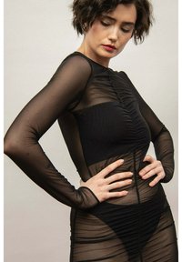 Czarna sukienka z długim rękawem, wykonana z przezroczystej siateczki, z marszczeniami, subtelną fakturą i dopasowanym krojem.