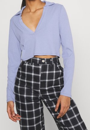Top a maniche lunghe ribbed di colore viola chiaro con scollo a V profondo e orlo cropped abbinato a pantaloni a quadri bianco e nero a vita alta con bottone.