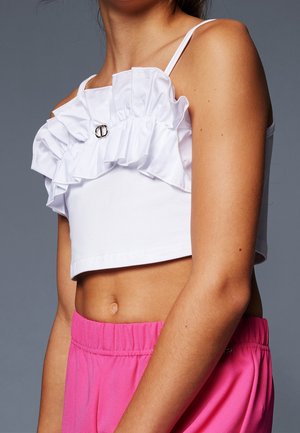 Witte cropped top met ruches bij de halslijn en zilveren hardware detail; gecombineerd met felroze broek met elastische tailleband.