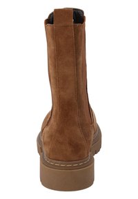Bottines en suède marron avec un dos haut, des panneaux élastiques sur les côtés et une semelle en caoutchouc épaisse. Présente un talon renforcé et un détail de couture apparente.