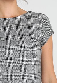 Top à manches courtes en motif à carreaux noir et blanc, avec un col rond et un tissu texturé agrémenté d'accents pied de poule.