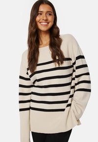 Cremefarbener gestreifter Pullover mit schwarzen horizontalen Streifen, der eine lockere Passform, einen weiten Ausschnitt und gerippte Bündchen aufweist. Das Material wirkt weich und strukturiert.