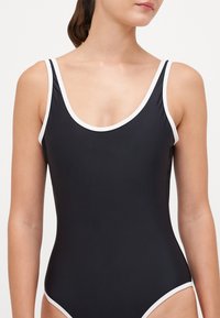 Schwarzes Badeanzug mit weißem Besatz, mit einem runden Ausschnitt und breiten Trägern. Hergestellt aus glattem, dehnbarem Material. Niedrig geschnittene Beinausschnitte.
