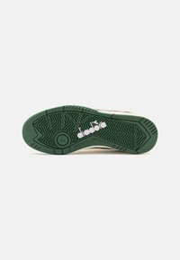 Suola di scarpa in gomma verde con scanalature testurizzate e un logo bianco. La forma è atletica, progettata per la presa e la durata.