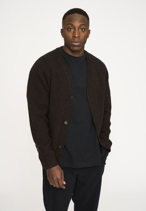 Brun rygstrikket cardigan med en afslappet pasform, der har en v-udskæring og fem knapper foran, båret over en sort t-shirt. Enkel design og tekstur.