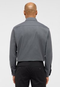 Grau gemustertes Langarmhemd mit strukturiertem Kragen und Knopfmanschetten, kombiniert mit dunklen maßgeschneiderten Hosen, von hinten betrachtet.