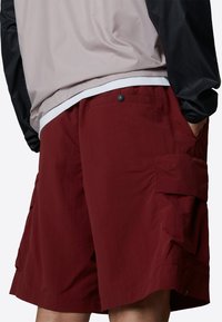 Burgundy cargo shorts made of lightweight fabric, featuring side pockets, a front button closure, and a relaxed fit design.